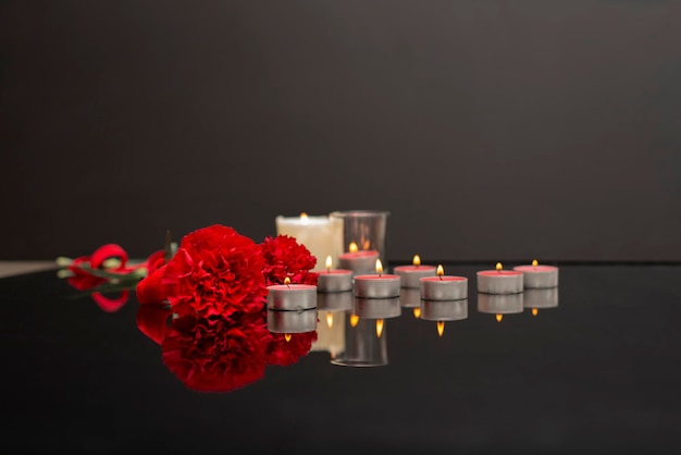 Photo red flowers carnation and many burning candles on a black surface selective focus on the one candle