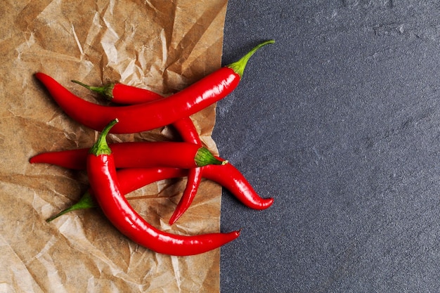 Red fresh chili peppers on parchment and slate background