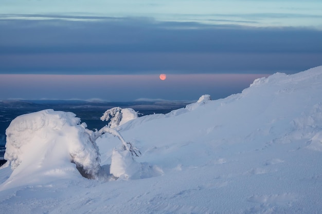 Red full cold moon over a snow-covered slope. Winter polar landscape. Cold winter weather. Harsh northern climate. Minimalistic view.