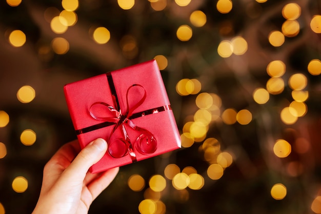 Red gift box in childrens hands on a Christmas background