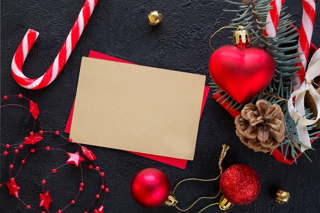 Red gift box with a Christmas toy in the shape of a heart, fir branches, christmas candy, garland and card for congratulatory text  on the black background