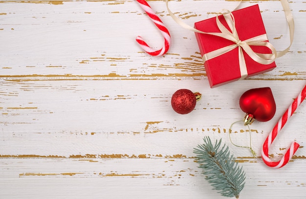 Red gift box with a Christmas toy in the shape of a heart, fir branches, christmas candy, garland on wooden background