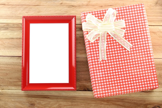 Red gift box with empty wooden picture frame on wood background.