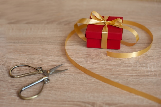 Red gift box with gold ribbon and scissors lie on the table