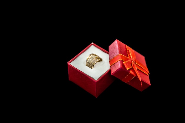 Red gift box with golden ring on black background