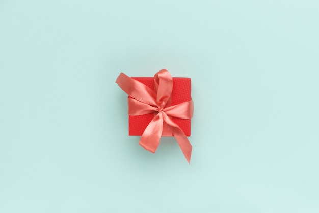 Red gift box with satin coral bow on top on a pastel turquoise. 