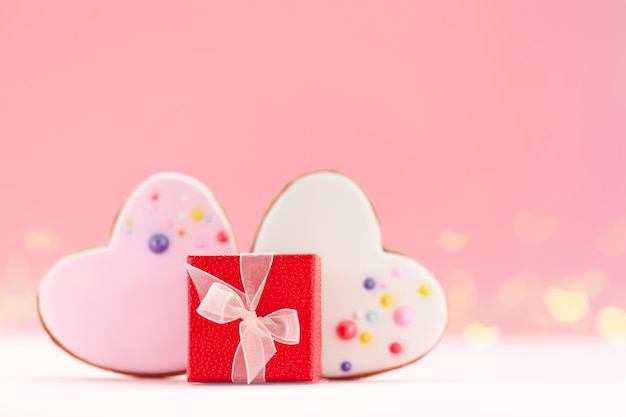 Red gift box with two hearts shaped gingerbread for Valentines Day, Mother Day or Birthday on pink background.