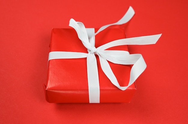 Red gift with white ribbon on red surface.