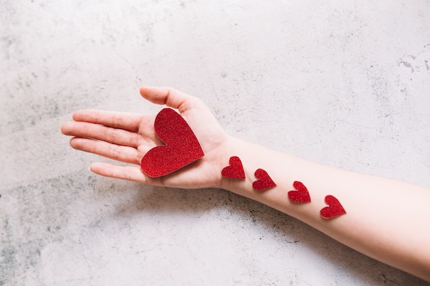 Red glitter heart shaped cardboard on the hand and small hearts on white surface. Love and valentines day concept.