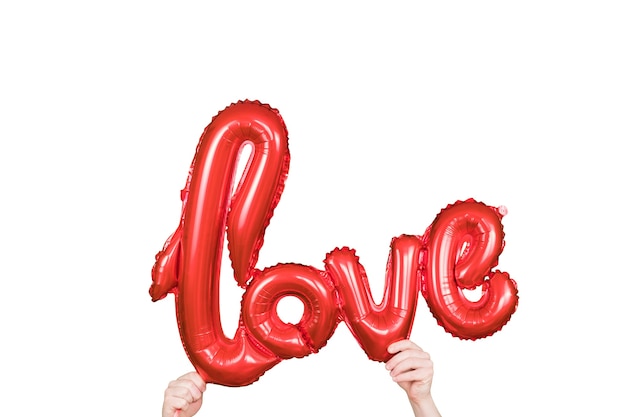 Photo red golden word love made of inflatable balloons in hands. red foil balloon letters, concept of romance.