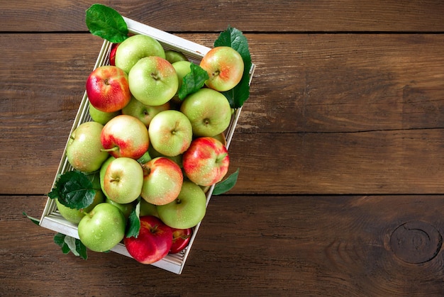 Red and green apples in wooden box on wooden table top view with copy space