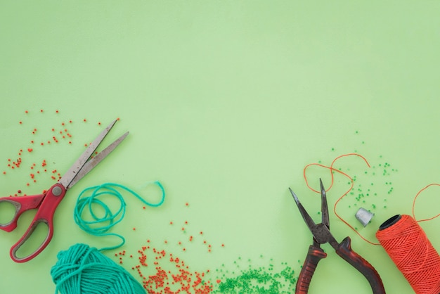 Red and green beads; scissor; pliers and spool on green background