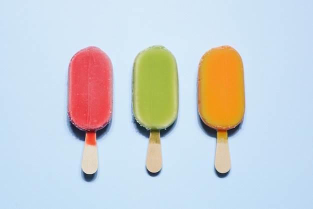 Red, green and orange frozen vegan sorbet ice creams on stick on light blue background