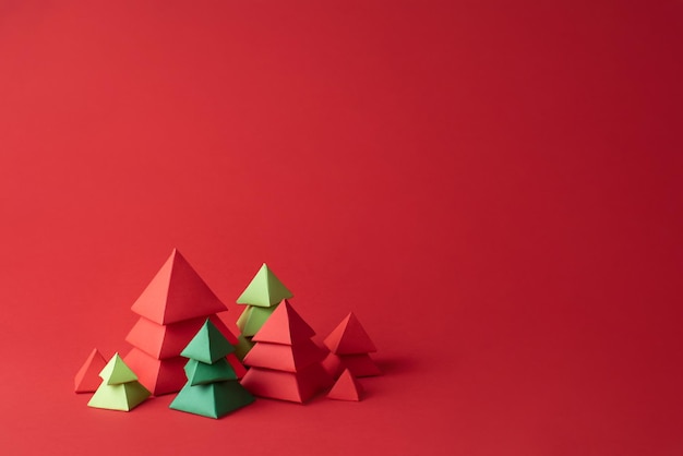 Red and green paper christmas trees on red background, paper crafts, Christmas concept, copy space.