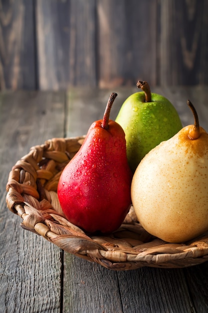 Red, green, yellow, sweet pear and an apple on a plate made of rattan on a dark