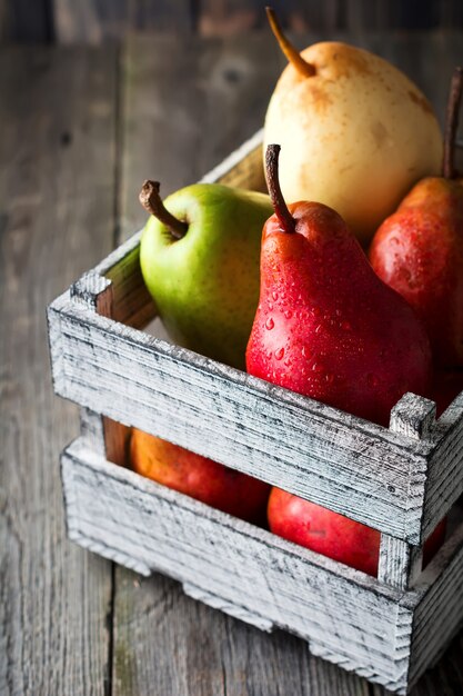 Red, green, yellow, sweet pear and one apple in the old wooden box on a dark