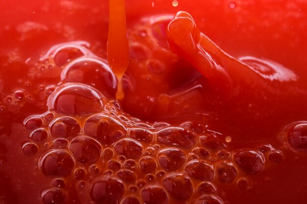 Red grocery background of tomato juice with splashes and bubbles close-up