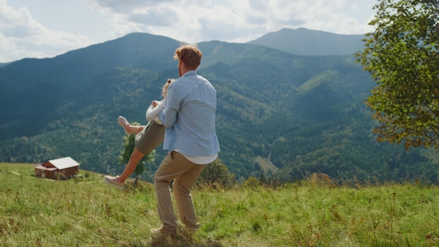 Red hair joyful father having fun circling cute daughter on green meadow Happy man playing with little girl in summer mountains Playful guy holding lovely child on hands enjoying holiday together