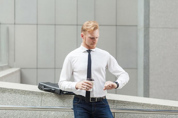 Red haired businessman looking at smart watch and holding cup