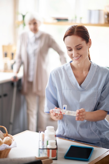 Photo red-haired caregiver sitting and organizing pills for patient