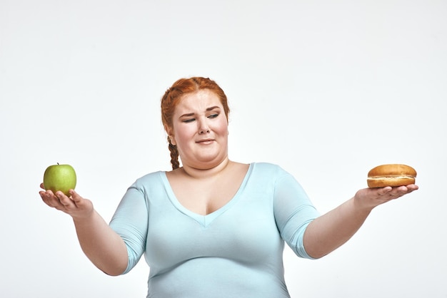 Red haired chubby woman is choosing between apple and sandwich