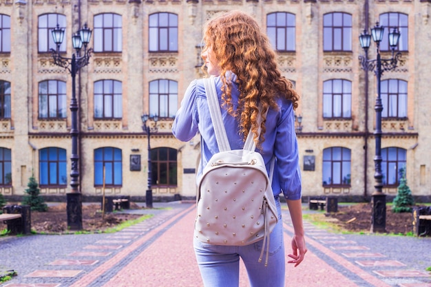 A red-haired, curly-haired student with a backpack on her back 