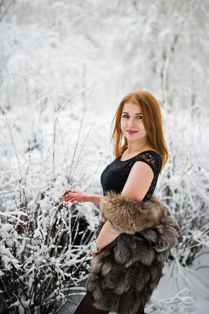 Red haired girl in fur coat walking at winter snowy park.