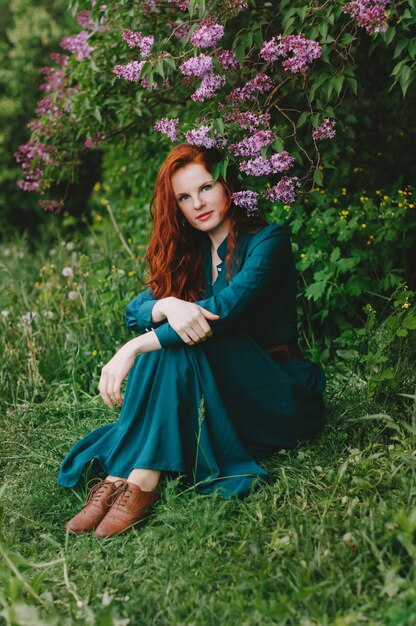 The red-haired girl is standing near the lilac bush