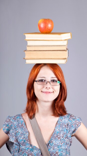 Red-haired girl keep apple and books on her head.