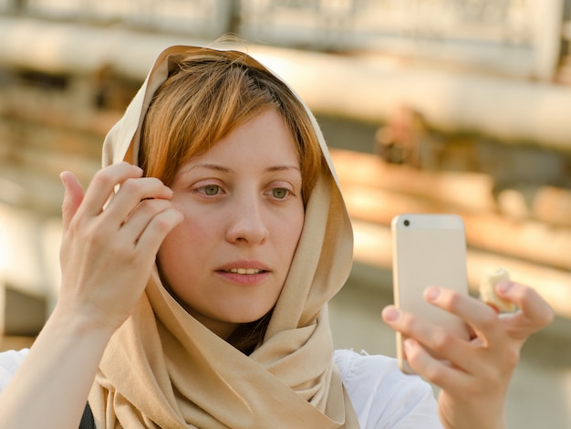 Red-haired girl in a palant makes selfie on phone, daylight