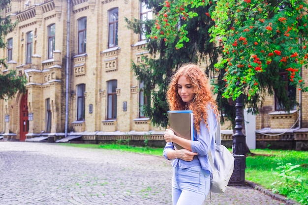 Red-haired girl student with folders and teaching materials in hands 