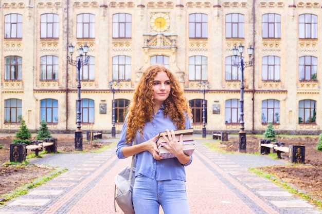 Red-haired girl student with a pile of books coming from the university library