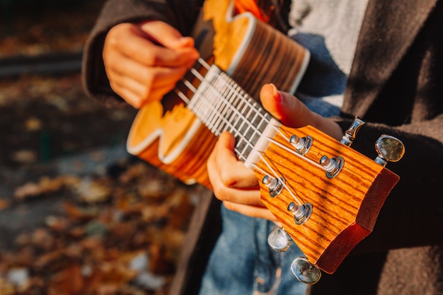 Red-haired girl with long hair plays on the ukulele in the park. School, music education concept, student learns to play the string instrument. Hands of a musician, classical, melody, creativity.