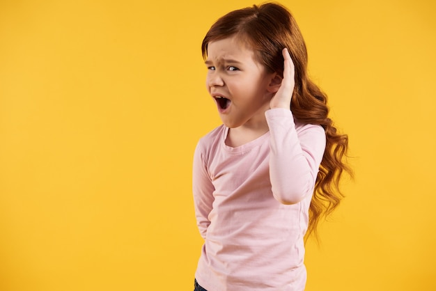 Red haired little girl puts hand to ear.