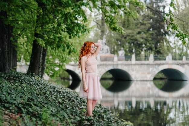 Red-haired young woman walking in a park with big white mansion