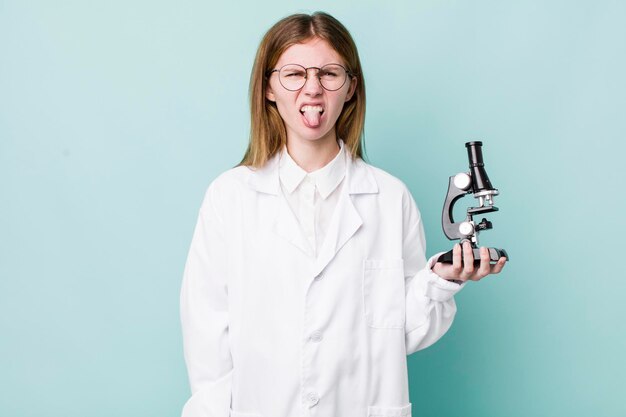 Red head pretty woman feeling disgusted and irritated and tongue out scientist with microscope concept