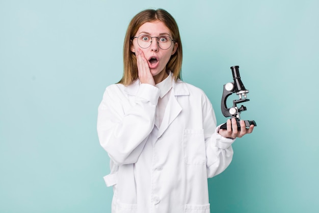 Red head pretty woman feeling shocked and scared scientist with microscope concept