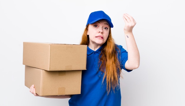 Red head pretty woman making capice or money gesture telling you to pay shipping boxes concept