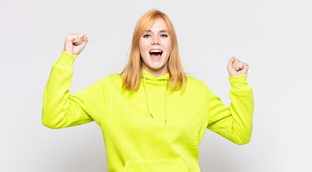 Red head pretty woman shouting triumphantly, looking like excited, happy and surprised winner, celebrating