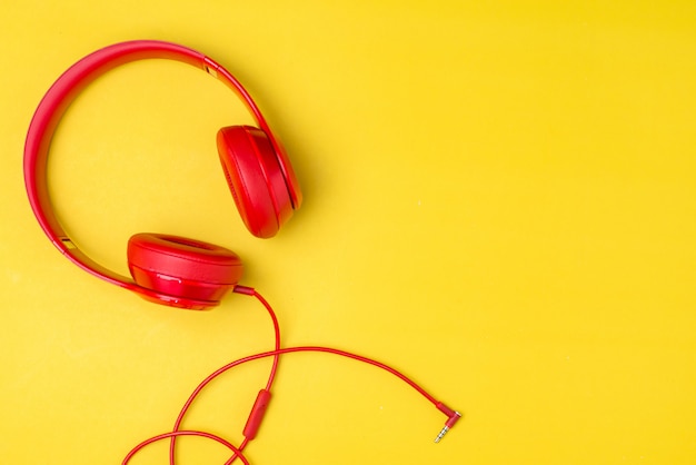 Red headphones listens to music on smartphone over yellow background.