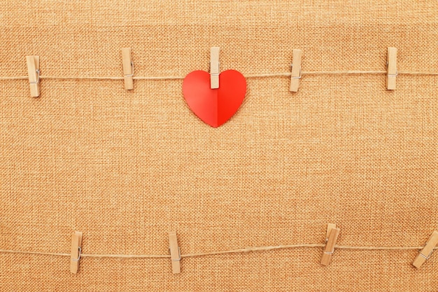 Red heart on clothes pin on brown textile background