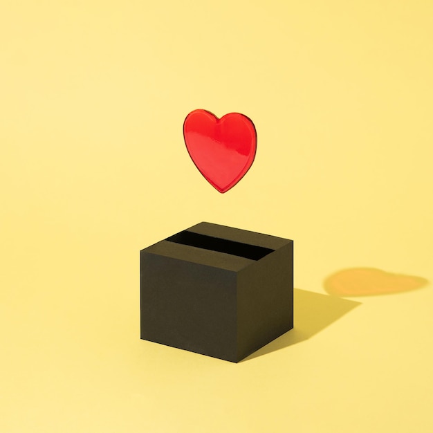 Red heart comes out of a black box and floats on a yellow background Valentines Day Abstract