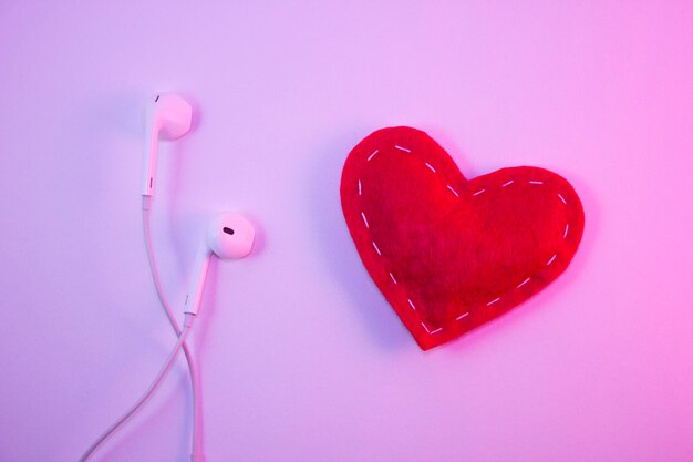 Red heart fabric with white threads and white headphones on a white background with pink light. Music concept, favorite music