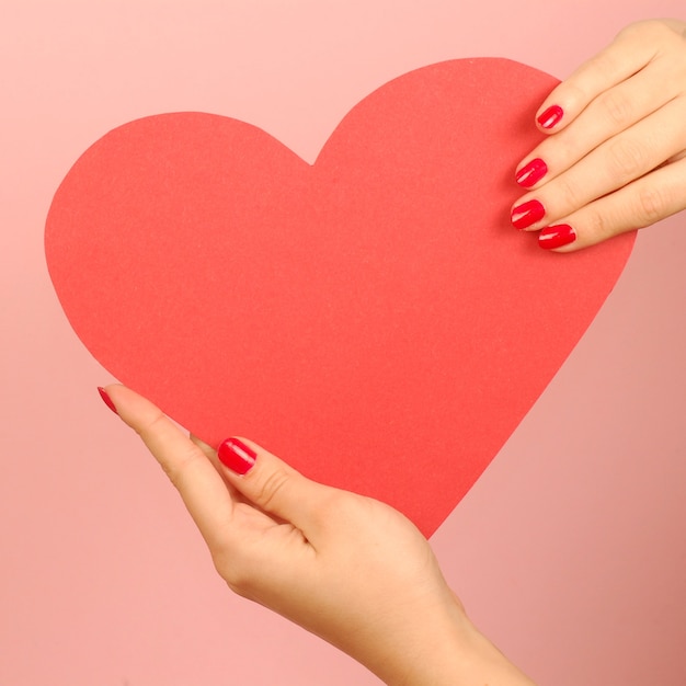 Red heart from paper in hands on red background.