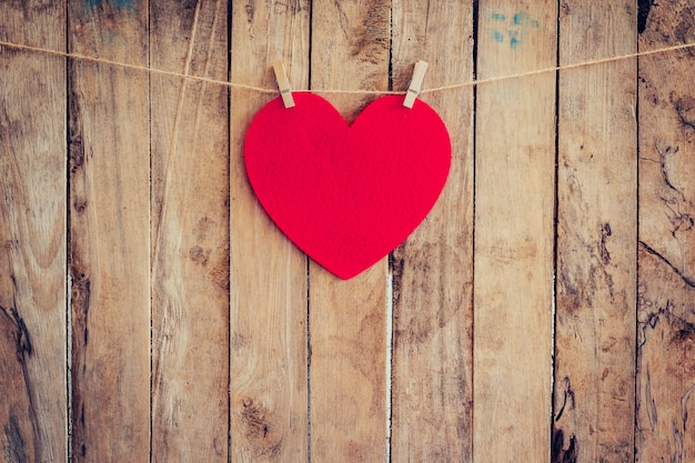 Red heart hanging on clothesline and rope with wooden background