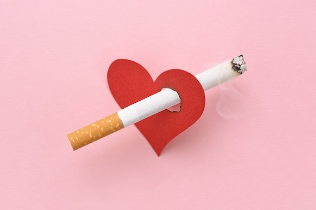 A red heart impaled by a burning cigarette, the harm of smoking, destroying health.