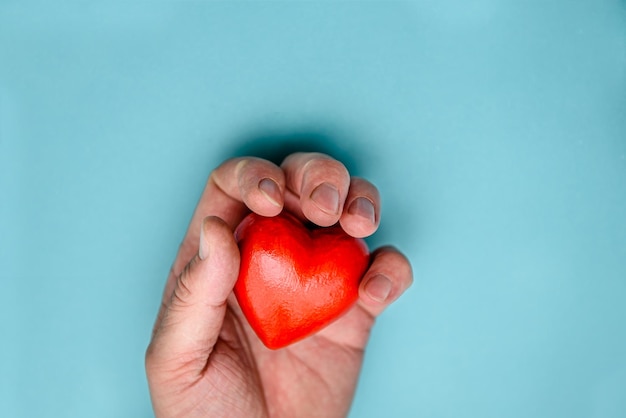 The red heart is squeezed by a man's hand Top view on a blue background