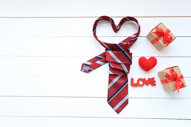 Red heart necktie and gift box with red ribbon and handmade crochet heart on wood background for happy fathers day 