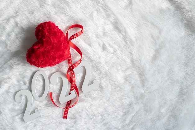 Red heart ribbon on New Years Day 2022 lying on light white fabric background top view