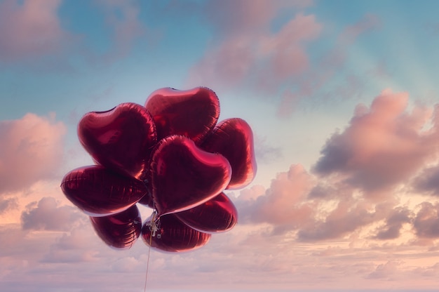 Red heart-shaped balloons with dramatic sky in vintage style, concept of love and valentine. Love is in the air